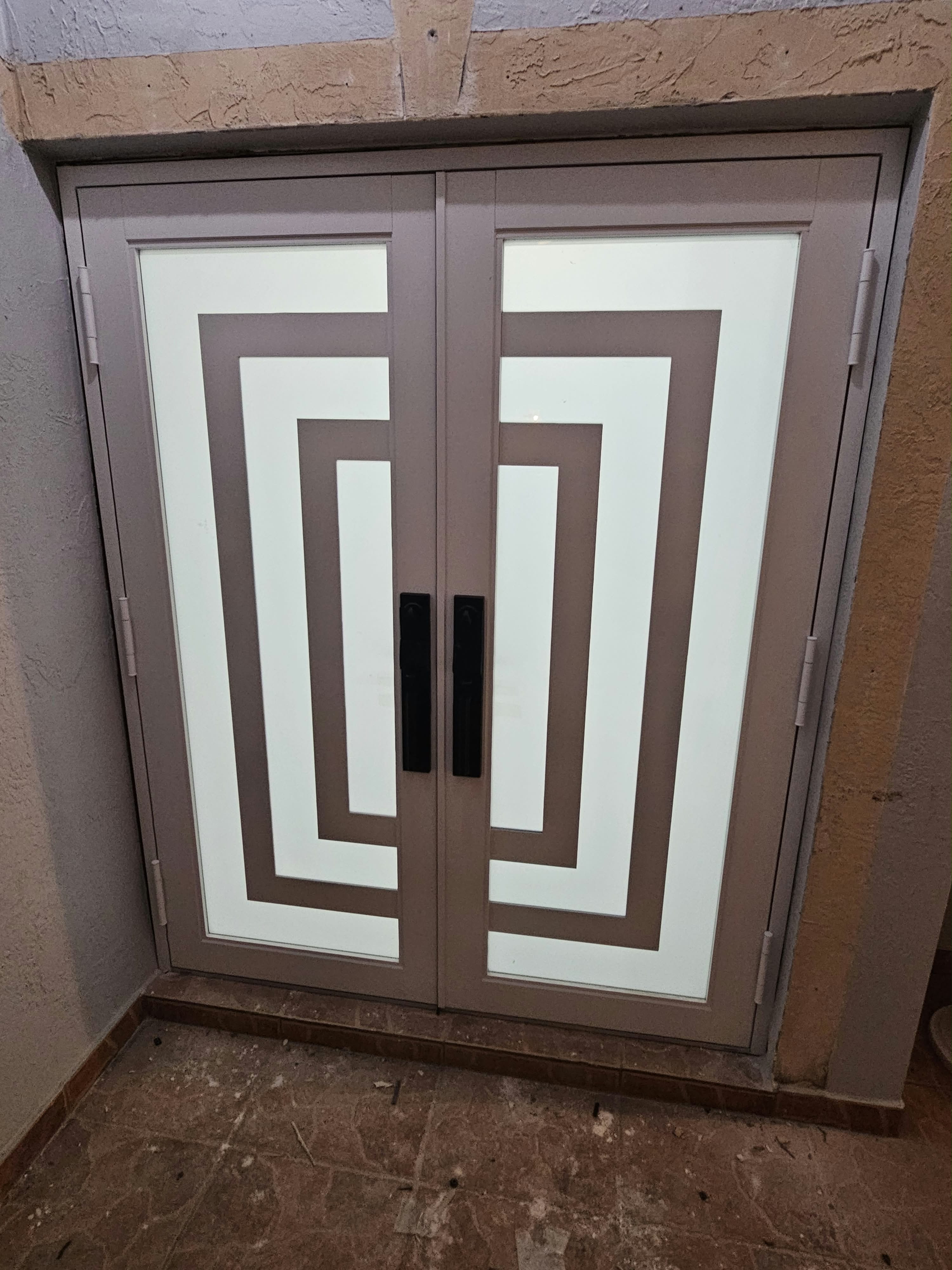 Después: Puerta doble de madera reemplazada por una puerta doble contra impacto con diseño geométrico y vidrio esmerilado. Misma abertura, ajuste estructural y terminación incluidos.